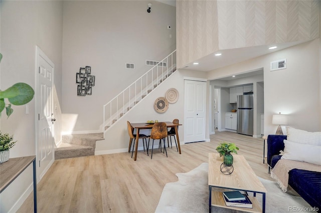 living area featuring a towering ceiling, stairway, light wood-style flooring, and visible vents