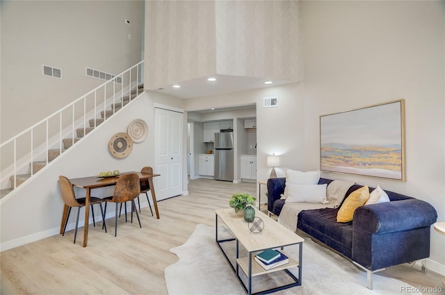 living area featuring light wood-style floors, visible vents, and stairway