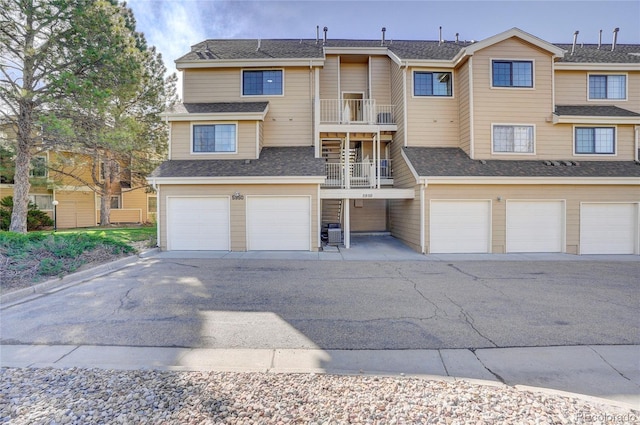 multi unit property featuring central AC, roof with shingles, a balcony, and an attached garage