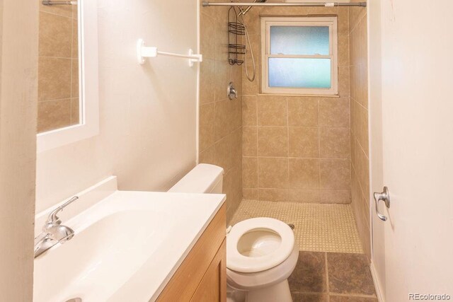 bathroom with a tile shower, toilet, tile patterned floors, and vanity