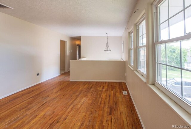 empty room with plenty of natural light, a textured ceiling, and hardwood / wood-style flooring