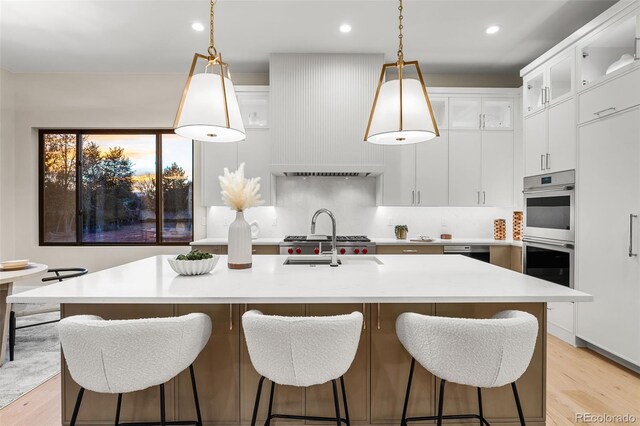 kitchen featuring white cabinets, an island with sink, decorative light fixtures, and light hardwood / wood-style floors