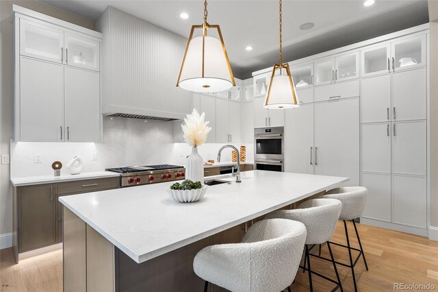 kitchen with pendant lighting, white cabinetry, double oven, and an island with sink