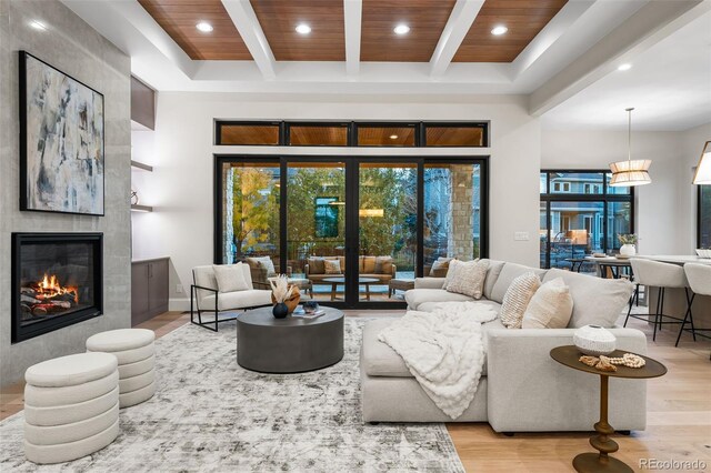 living room featuring beam ceiling, a tile fireplace, wooden ceiling, and light hardwood / wood-style floors