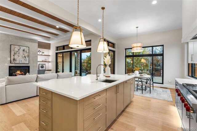 kitchen with a kitchen island with sink, sink, hanging light fixtures, beamed ceiling, and a tiled fireplace