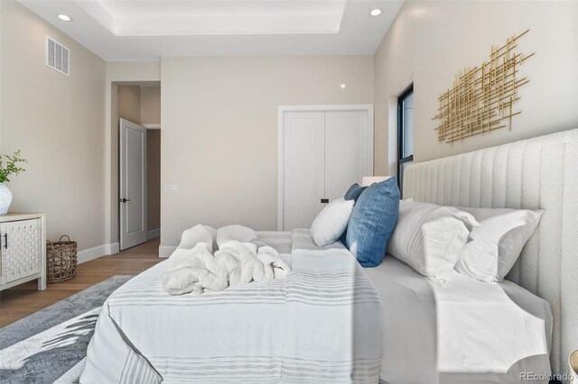 bedroom with hardwood / wood-style floors, a raised ceiling, and a closet