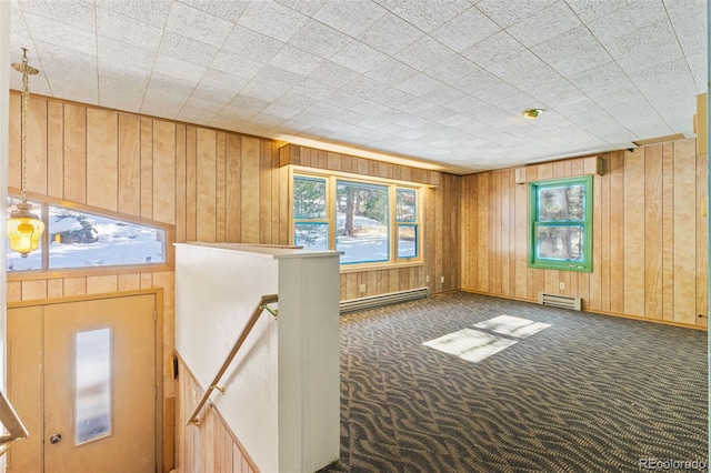 spare room featuring baseboard heating, wooden walls, and dark colored carpet