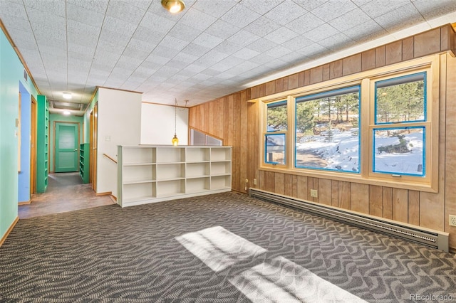 empty room featuring dark colored carpet, wood walls, and baseboard heating