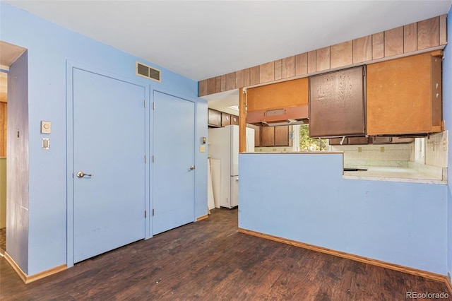 kitchen with tasteful backsplash, kitchen peninsula, dark wood-type flooring, and white refrigerator