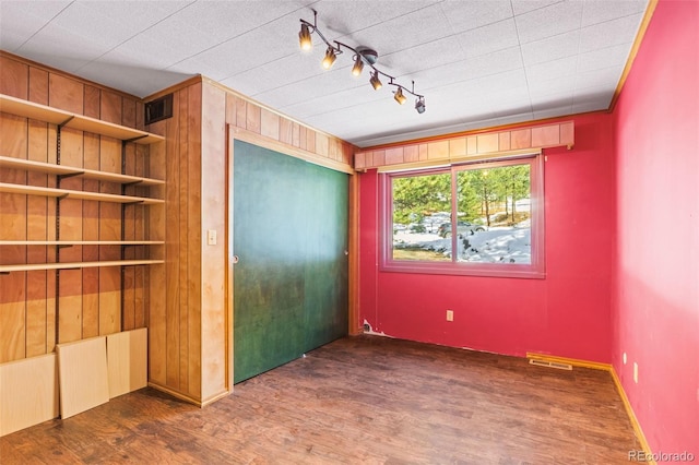 unfurnished bedroom with rail lighting, dark wood-type flooring, and wooden walls