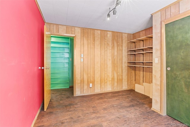 spare room with built in shelves, dark hardwood / wood-style flooring, rail lighting, and wooden walls