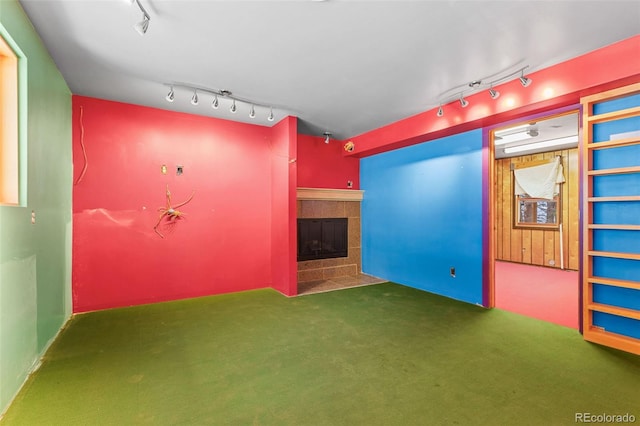 carpeted spare room featuring a tile fireplace and rail lighting