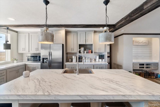 kitchen featuring light stone counters, a sink, appliances with stainless steel finishes, gray cabinets, and beam ceiling