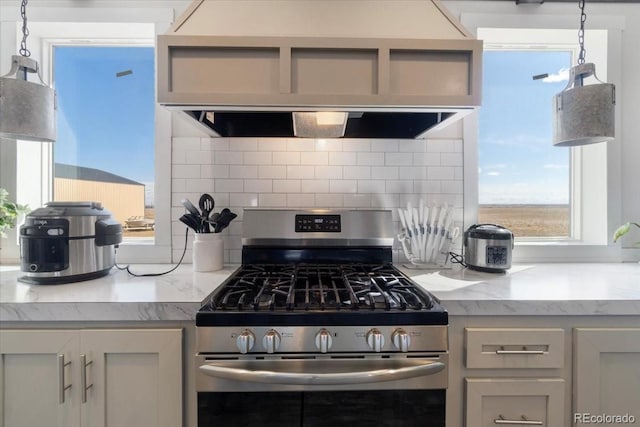 kitchen featuring light stone counters, stainless steel range with gas stovetop, backsplash, and wall chimney exhaust hood