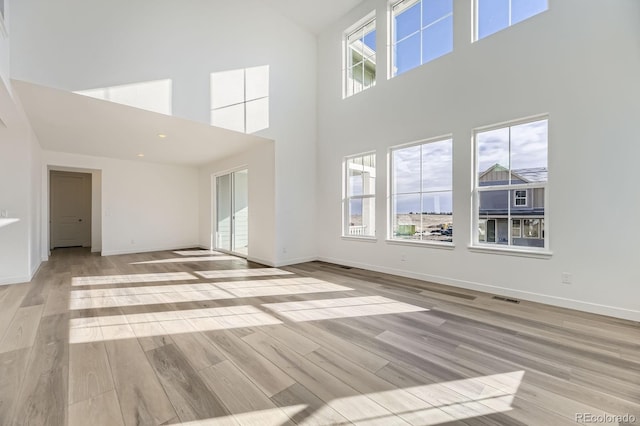 unfurnished living room with light wood-style flooring, a high ceiling, and baseboards