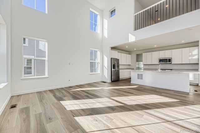 kitchen featuring visible vents, white cabinets, baseboards, light wood-style flooring, and stainless steel appliances