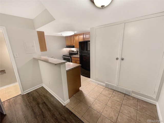 kitchen featuring stainless steel electric range, light tile patterned flooring, kitchen peninsula, and refrigerator