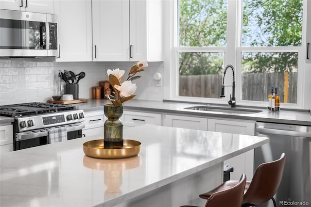 9220 Yucca Way, Thornton, CO 80229 - kitchen featuring appliances with stainless steel finishes, a sink, white cabinetry, decorative backsplash, and light stone counters