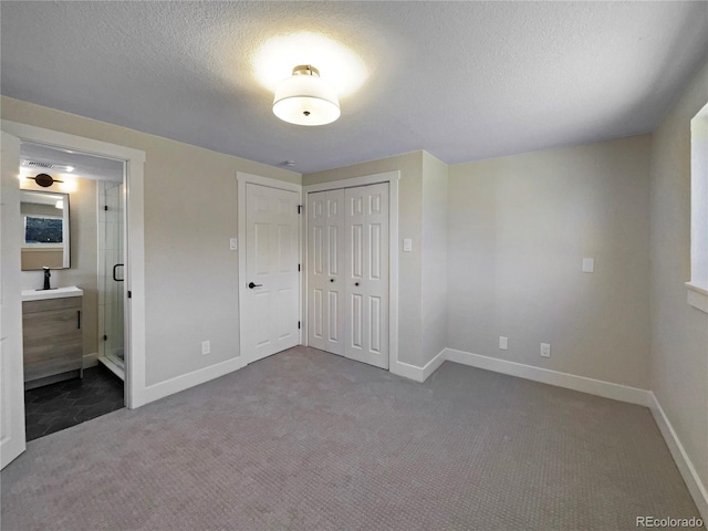 unfurnished bedroom with carpet flooring, ensuite bathroom, a textured ceiling, sink, and a closet