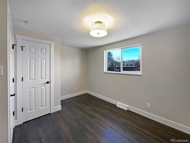 spare room featuring a textured ceiling and dark wood-type flooring