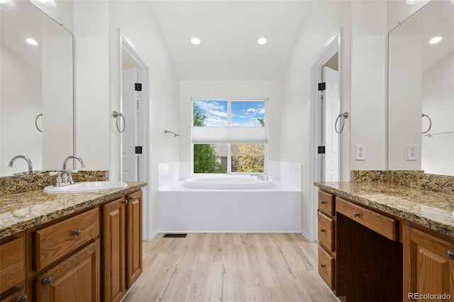 7837 Aravon Ct, Lone Tree, CO 80124 - bathroom featuring wood finished floors, a garden tub, two vanities, recessed lighting, and vaulted ceiling