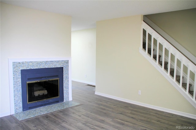 unfurnished living room with wood finished floors, visible vents, baseboards, stairs, and a tiled fireplace