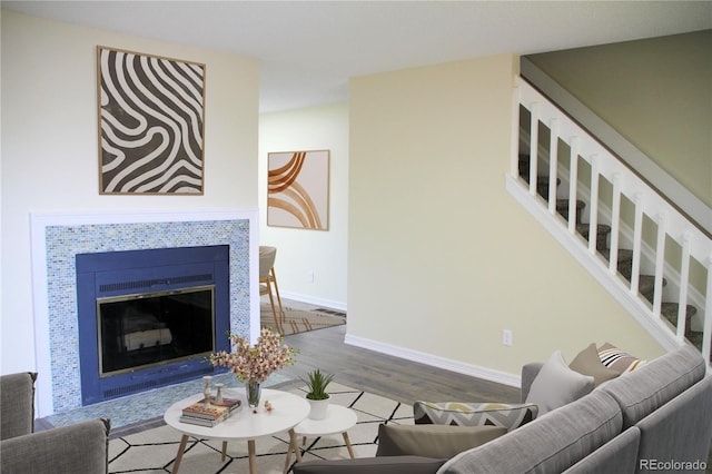 living room featuring visible vents, a tiled fireplace, wood finished floors, baseboards, and stairs