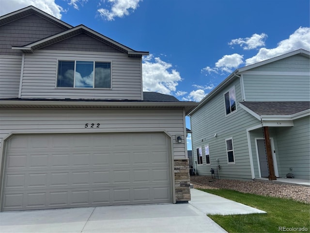 522 Foxtail Pl, Wiggins, CO 80654 - view of side of property with driveway, an attached garage, stone siding, and a shingled roof