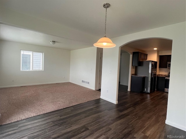 522 Foxtail Pl, Wiggins, CO 80654 - unfurnished living room with arched walkways, baseboards, and dark wood-style flooring