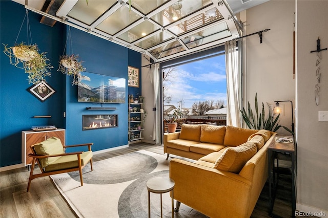 living area with baseboards, wood finished floors, and a glass covered fireplace