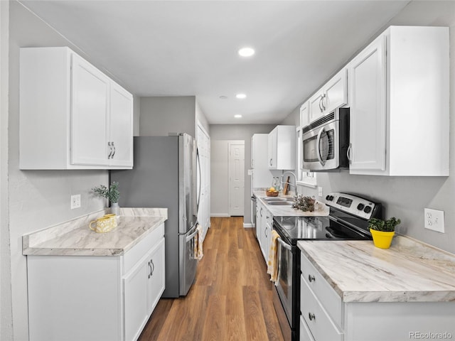 kitchen featuring appliances with stainless steel finishes, white cabinetry, wood finished floors, recessed lighting, and a sink