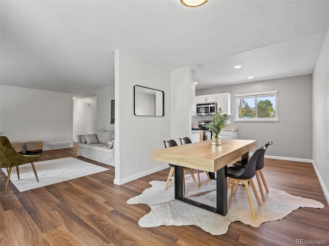 dining room featuring baseboards, a textured ceiling, wood finished floors, and recessed lighting