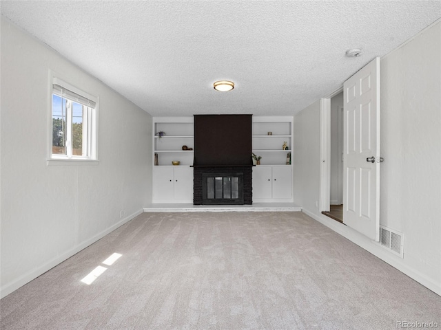 unfurnished living room featuring built in shelves, carpet flooring, a textured ceiling, a brick fireplace, and baseboards