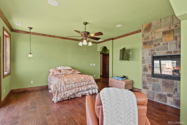 bedroom with a stone fireplace, ornamental molding, wood-type flooring, and ceiling fan