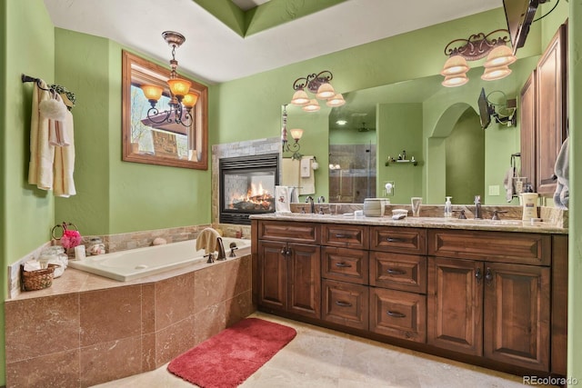 bathroom with a relaxing tiled bath, double sink vanity, a chandelier, tile floors, and a multi sided fireplace