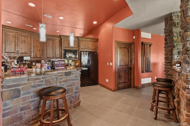 kitchen featuring black appliances, light stone counters, pendant lighting, light tile flooring, and a kitchen bar