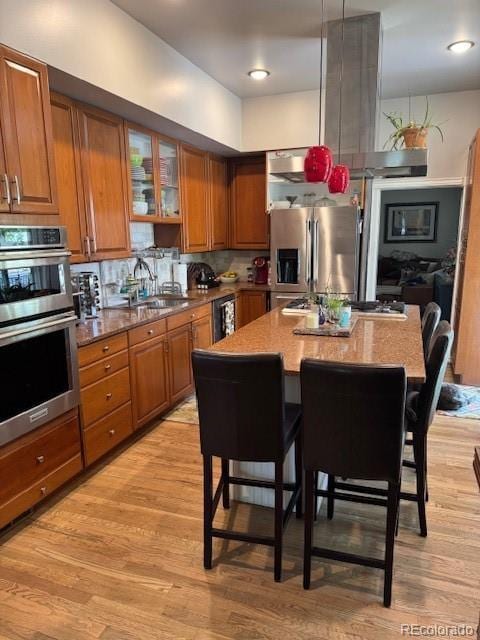 3098 W 39th Ave, Denver, CO 80211 - kitchen featuring appliances with stainless steel finishes, brown cabinetry, a breakfast bar, light wood-style floors, and recessed lighting