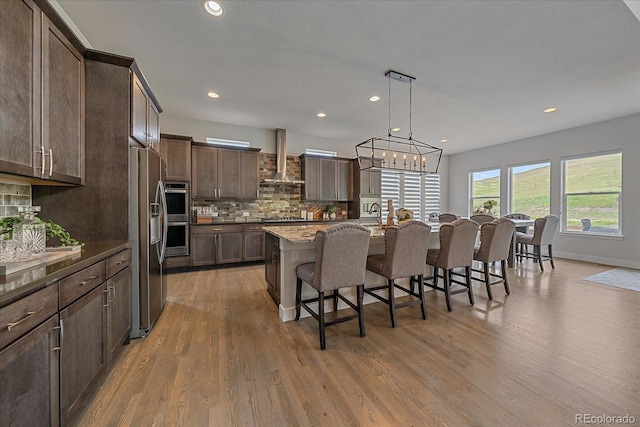9433 Torrey Way, Arvada, CO 80007 - kitchen with wall chimney range hood, a kitchen bar, wood finished floors, decorative backsplash, and stainless steel appliances