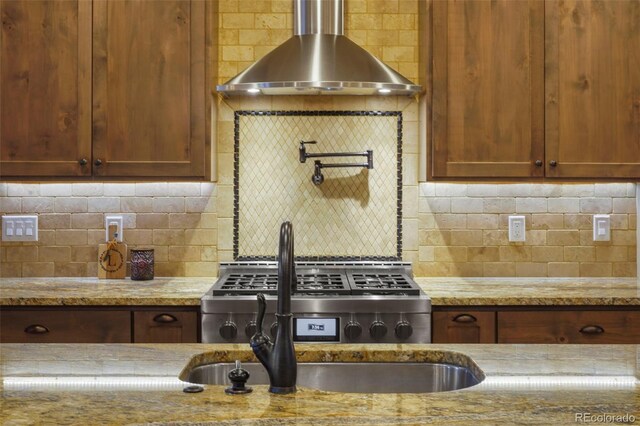 kitchen featuring decorative backsplash, stove, light stone countertops, and wall chimney exhaust hood