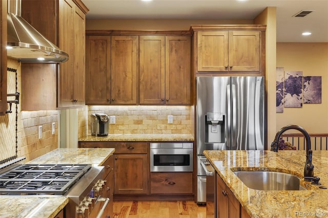 kitchen with appliances with stainless steel finishes, tasteful backsplash, sink, light stone counters, and wall chimney range hood