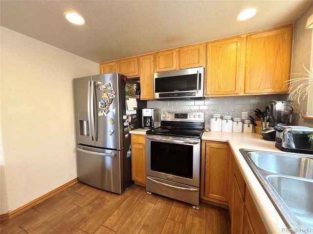 2835 S Tower Way, Aurora, CO 80013 - kitchen with appliances with stainless steel finishes, a sink, light countertops, light wood finished floors, and tasteful backsplash