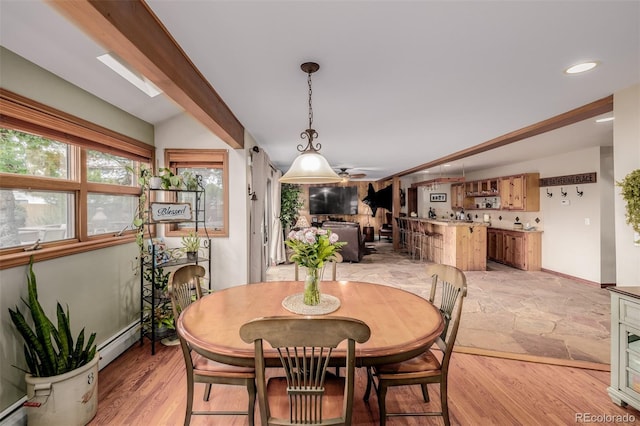 dining space with vaulted ceiling with skylight, stone finish flooring, baseboard heating, and recessed lighting