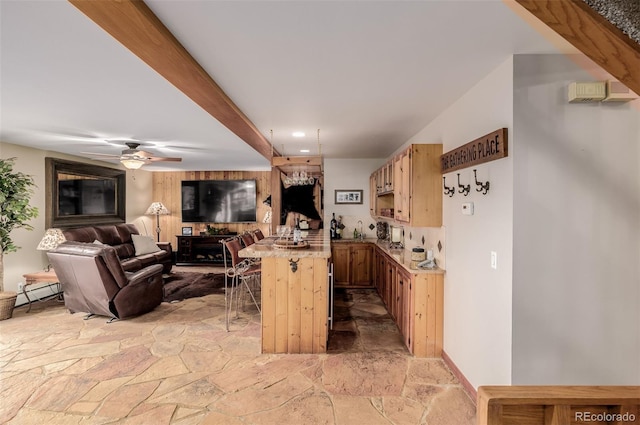 kitchen featuring open floor plan, stone finish flooring, a kitchen bar, and beam ceiling