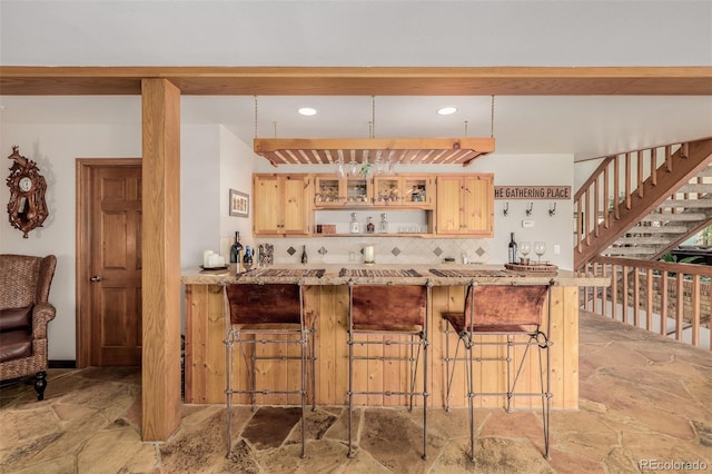 kitchen with stone finish flooring, backsplash, a kitchen bar, and light brown cabinets