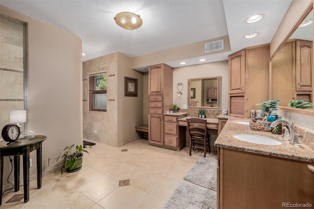 full bath featuring visible vents, vanity, a textured ceiling, a walk in shower, and baseboards