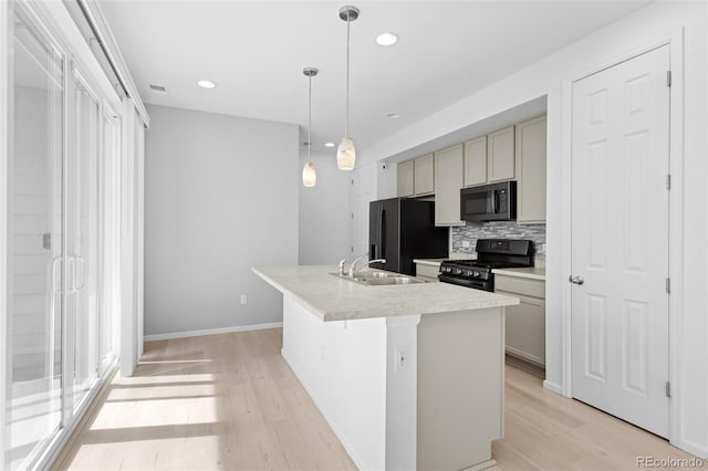 kitchen featuring a sink, light wood-style floors, black appliances, tasteful backsplash, and a center island with sink