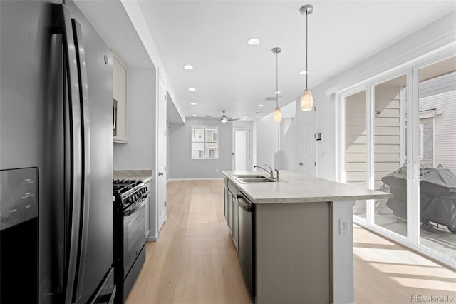 kitchen with a center island with sink, light countertops, light wood-style flooring, appliances with stainless steel finishes, and a sink