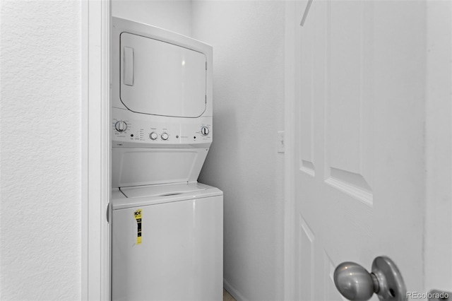 washroom with a textured wall and stacked washer and clothes dryer