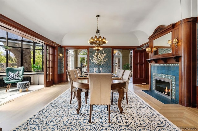 dining room featuring a tile fireplace, vaulted ceiling, light parquet flooring, and an inviting chandelier