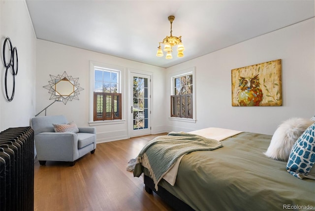 bedroom with an inviting chandelier, access to exterior, wood-type flooring, and radiator heating unit